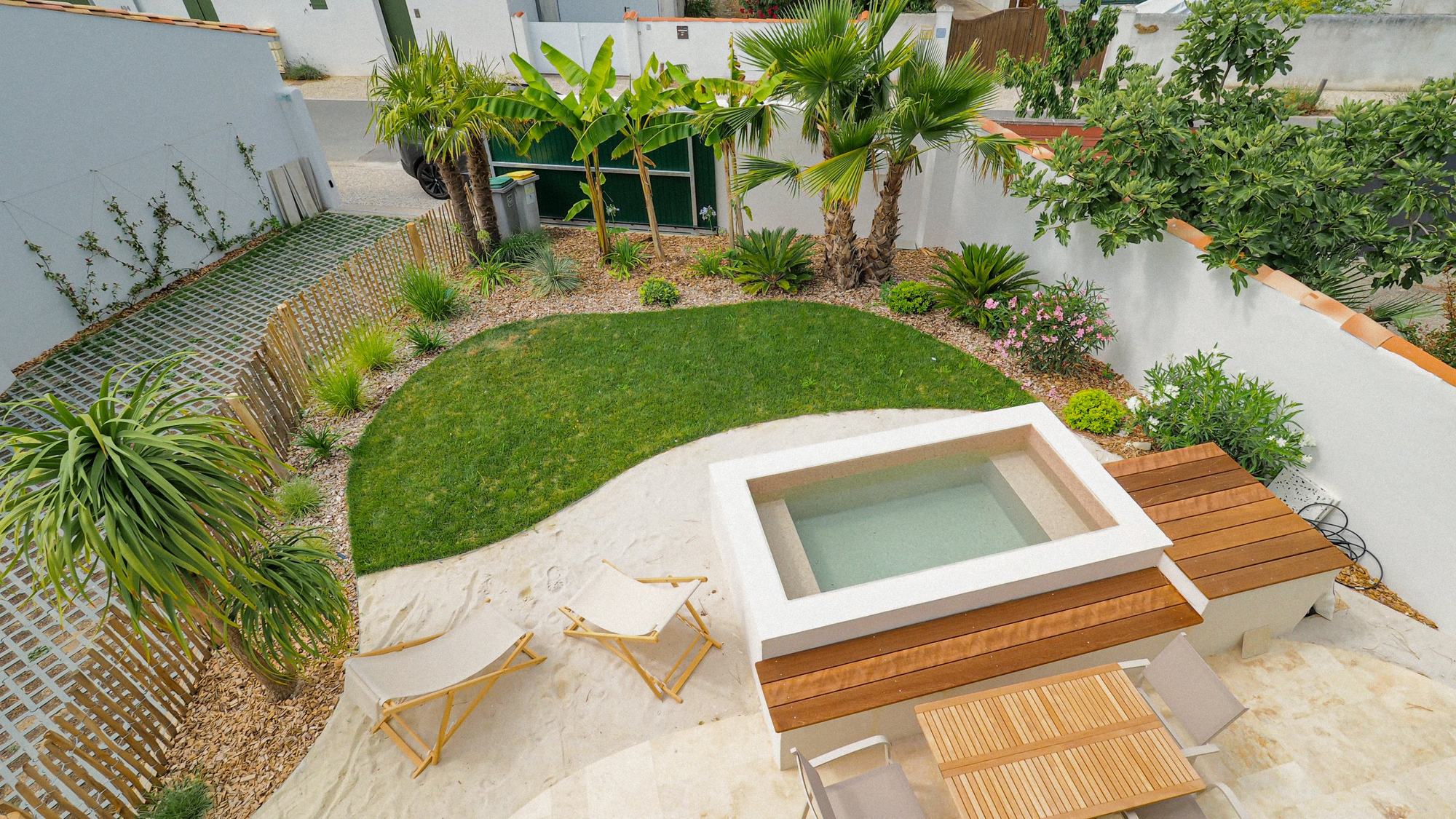 Jardin avec bassin, terrasse, pelouse en courbe, palmiers et ganivelle réalisé par AH Paysage